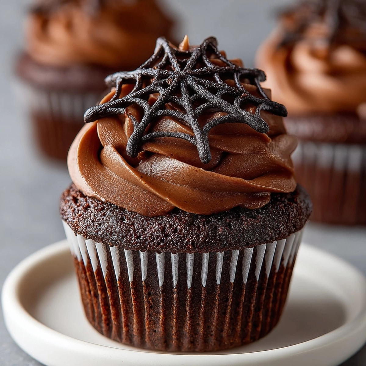 Elevated spider web cupcakes, frosted chocolate, adorned with delicate, hand-pulled sugar webs.
