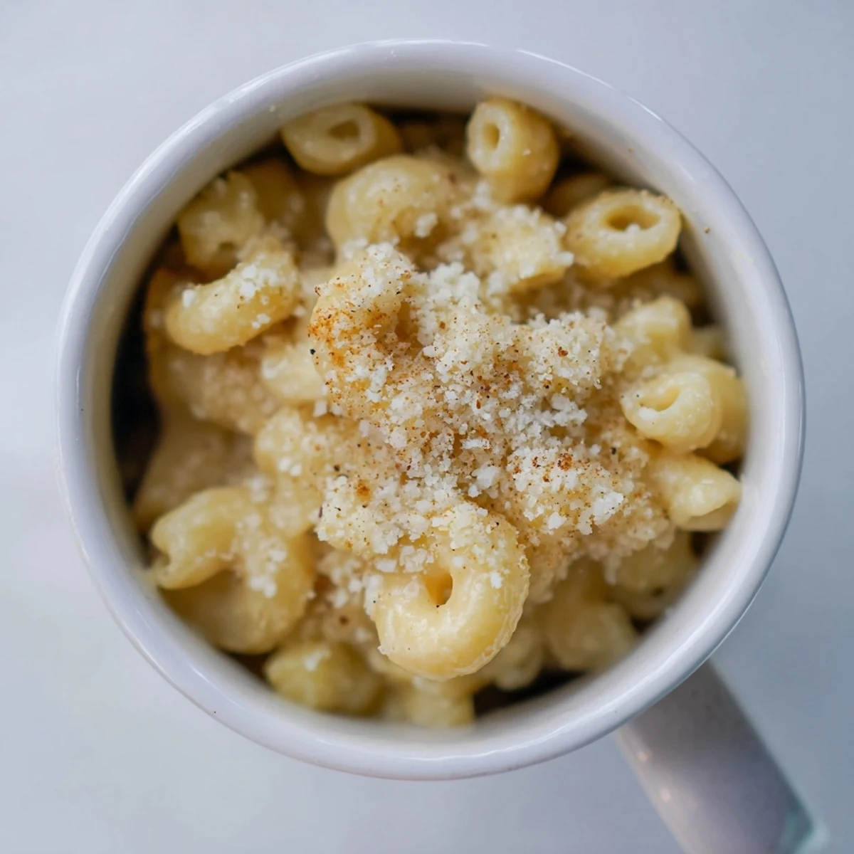 A close-up of golden Mug Mac & Cheese topped with parmesan and paprika, ready to eat.