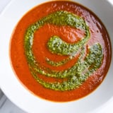Spoon dipping into a warm bowl of velvety tomato soup with a swirl of basil pesto, served with crusty artisan bread on the side.