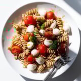 A vibrant Caprese Salad Pasta served as a light vegetarian main, finished with olive oil and optional balsamic glaze garnish.