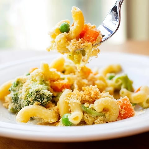 A close-up of golden Garden Veg Mac and Cheese with peas, carrots, and broccoli baked in a skillet.