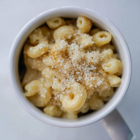 A close-up of golden Mug Mac & Cheese topped with parmesan and paprika, ready to eat.