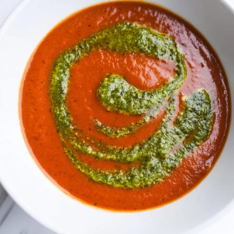 Spoon dipping into a warm bowl of velvety tomato soup with a swirl of basil pesto, served with crusty artisan bread on the side.