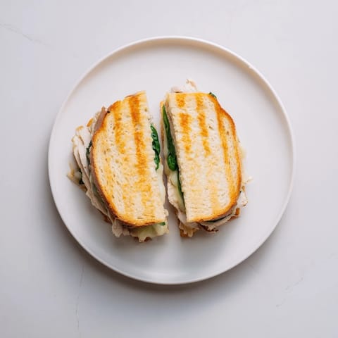 Savory grilled chicken spinach panini featuring melted cheese and garlic butter, served warm and cut in half.