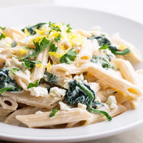 Steaming creamy feta spinach pasta in a skillet, spinach wilting into tangy cheese sauce for a quick vegetarian weeknight dinner.