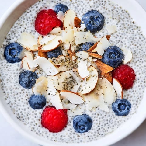 Vibrant poppy seed chia pudding topped with raspberries and coconut, served in a rustic ceramic bowl.