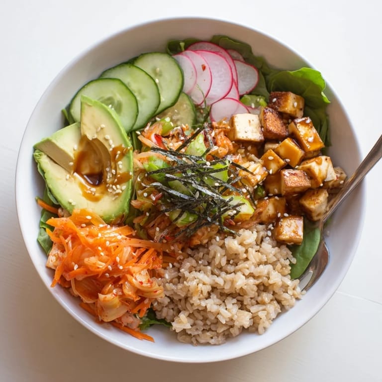 Colorful bowl featuring kimchi, seasonal vegetables, avocado, and savory dressing.  