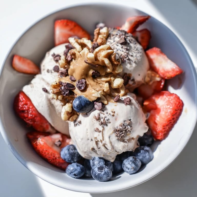 A layered image of a Protein Ice Cream Bowl with fresh berries, nuts, and a drizzle of peanut butter.
