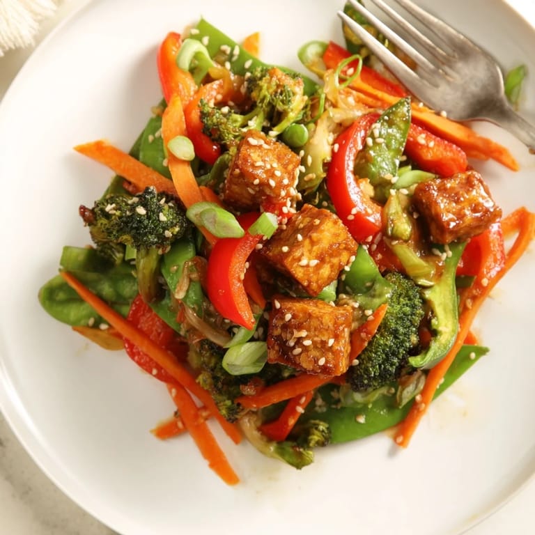 Colorful medley of bell peppers, broccoli, and carrots sizzling with tempeh in a savory Asian-inspired stir-fry, served over steamed rice.  